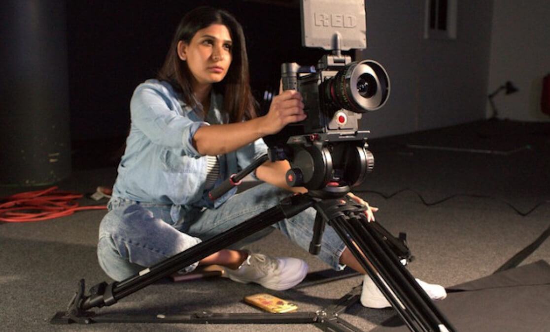 SAE film student Bushra Khanum sitting behind a RED camera on tripod with monitor display.