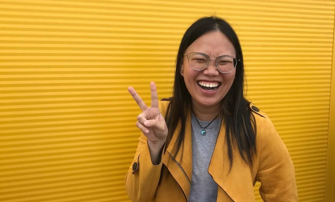 Woman smiling in front of yellow wall. Wearing yellow jacket