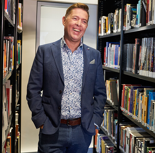 Man standing in library wearing a casual blue suit.