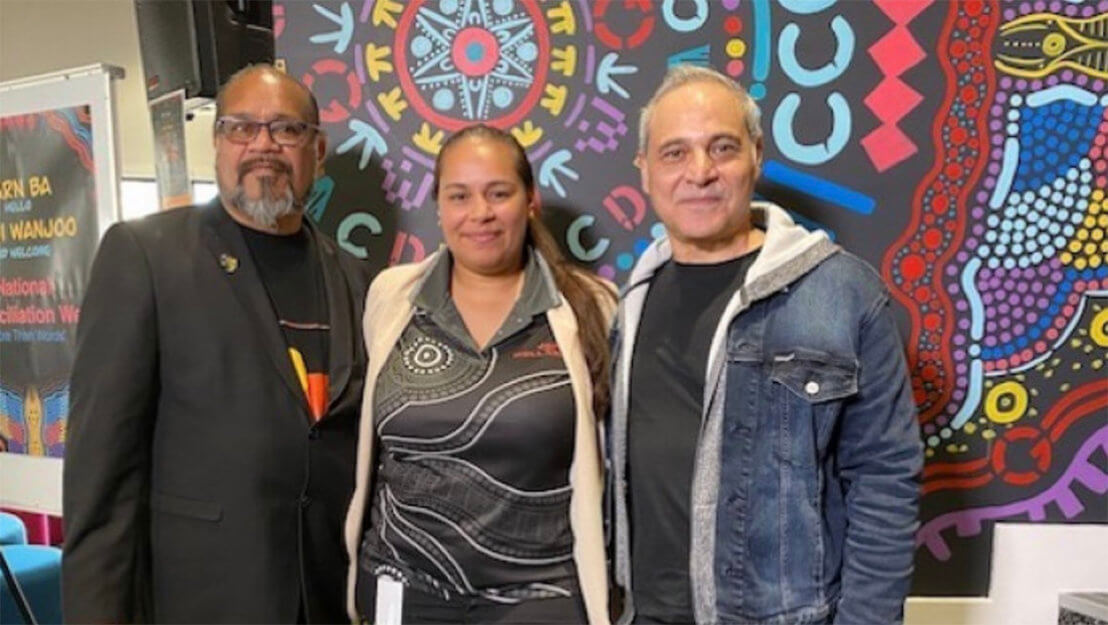 Two men and a woman standing in front of an aboriginal mural