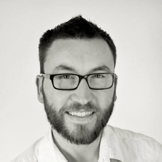 Man wearing square glasses. Smiling. Name, Adam Single