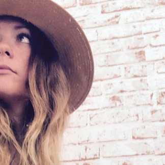 Woman wearing hat sitting in front of brick wall