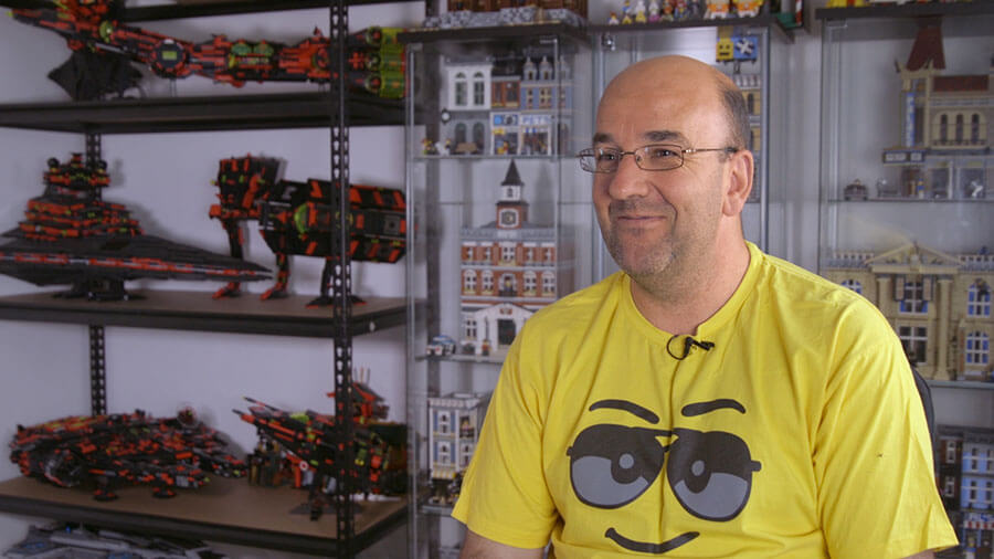 Man with mic on sits in front of shelves filled with various lego models