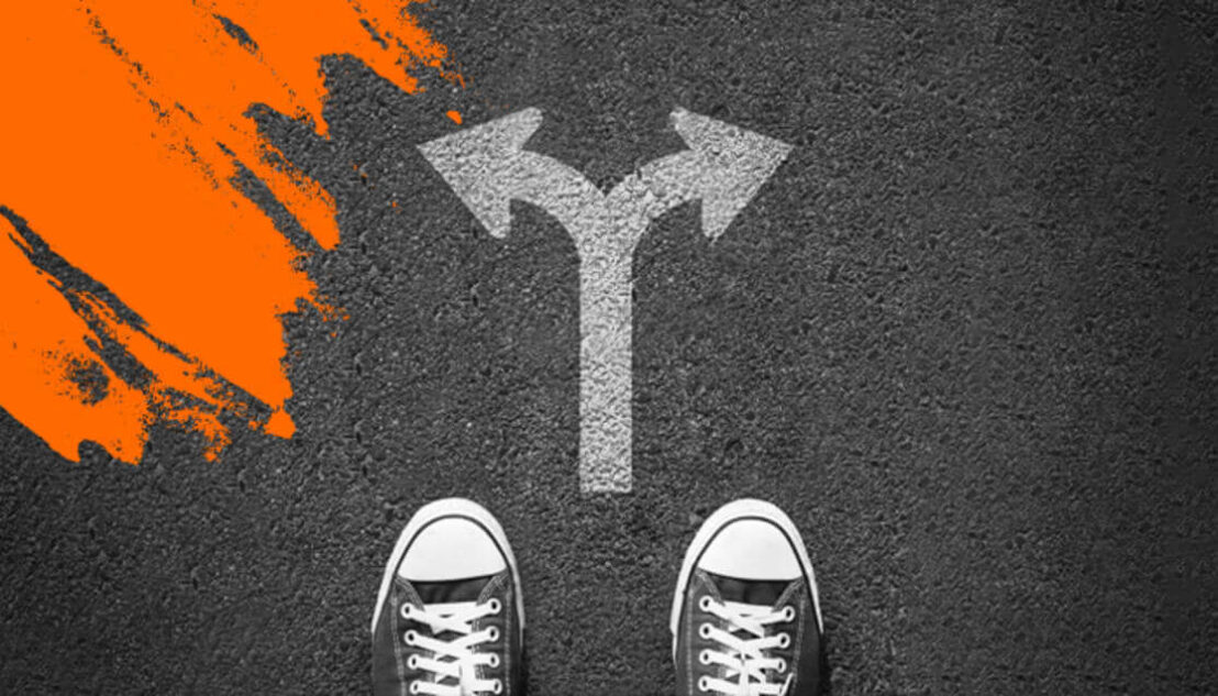 Feet with sneakers standing below a road arrow that's pointing both left and right