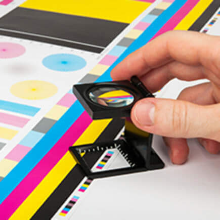 Person using magnifying glass over CMYK print