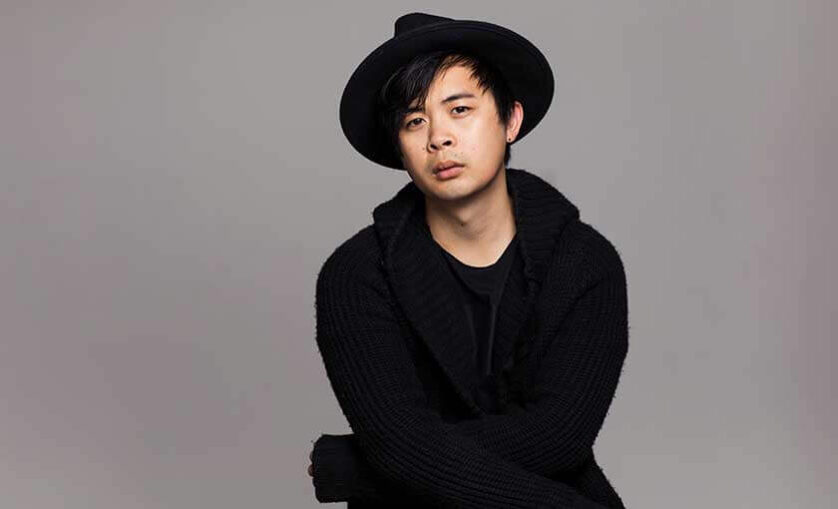 Man sits with arms crossed and wearing a hat. Alumni and game designer Keovilay Cola Saycocie