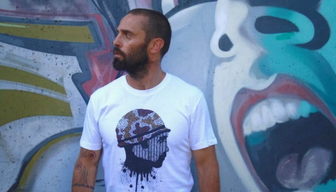 Man with beard wearing graphic tshirt. Standing in front of graffiti wall