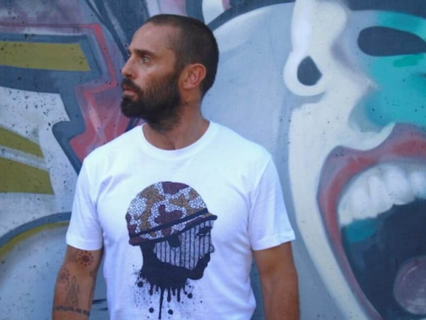 Man with beard wearing graphic tshirt. Standing in front of graffiti wall