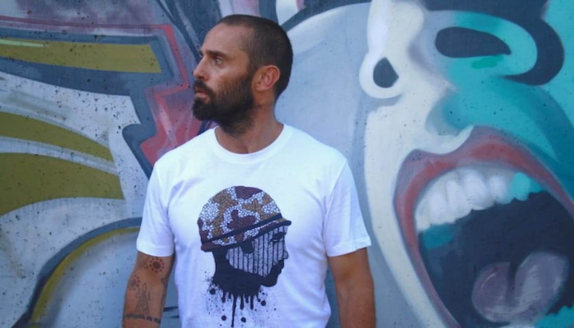 Man with beard wearing graphic tshirt. Standing in front of graffiti wall