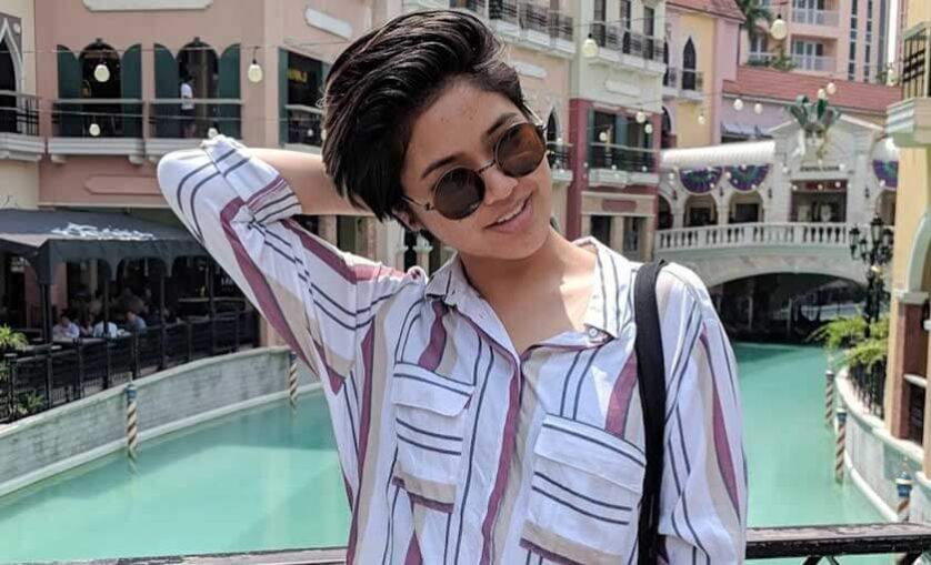 Woman stands on a bridge with arm up and behind head.