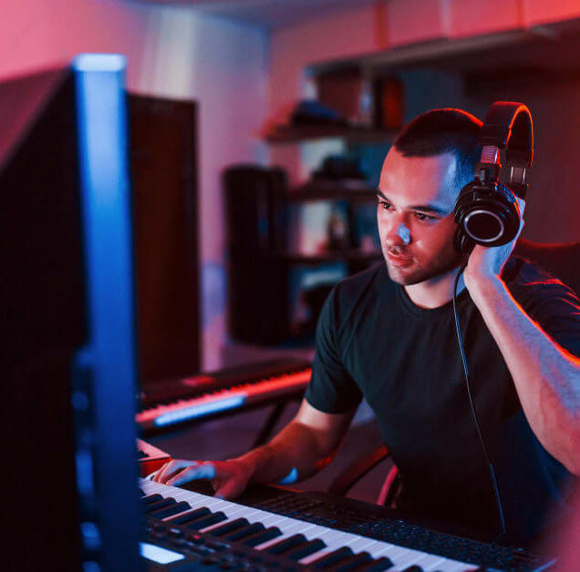 Student with headphones, keyboard in front of a screen in a studio