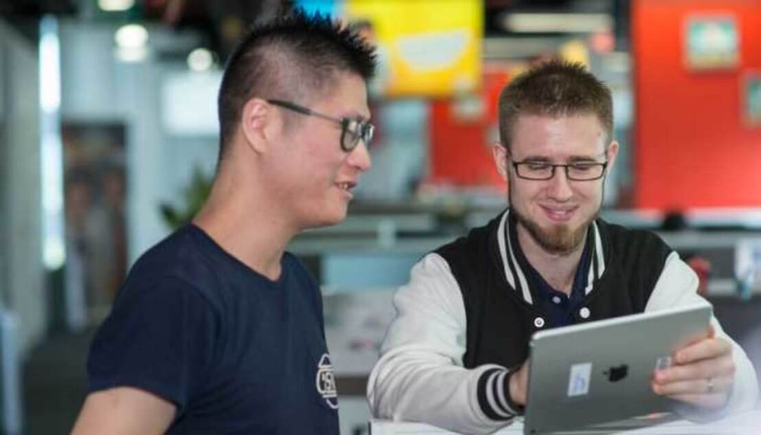 Two students working on a tablet, smiling. Ubisoft hires SAE graduate