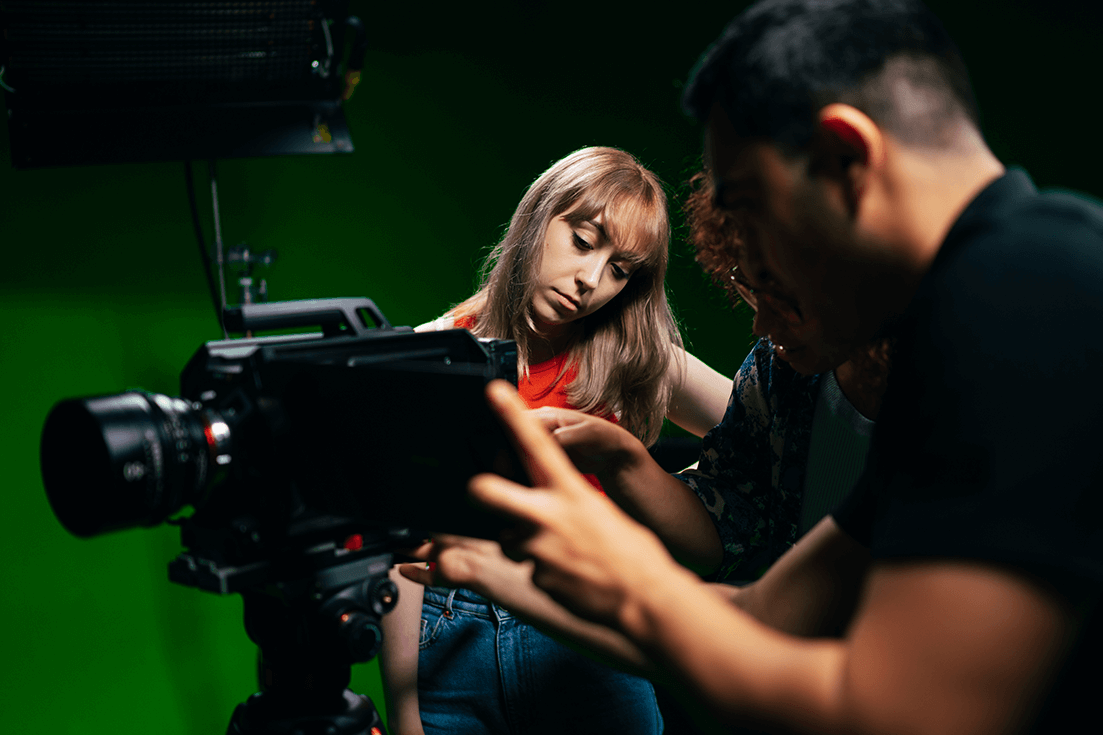 Film students looking at a camera on a green set.