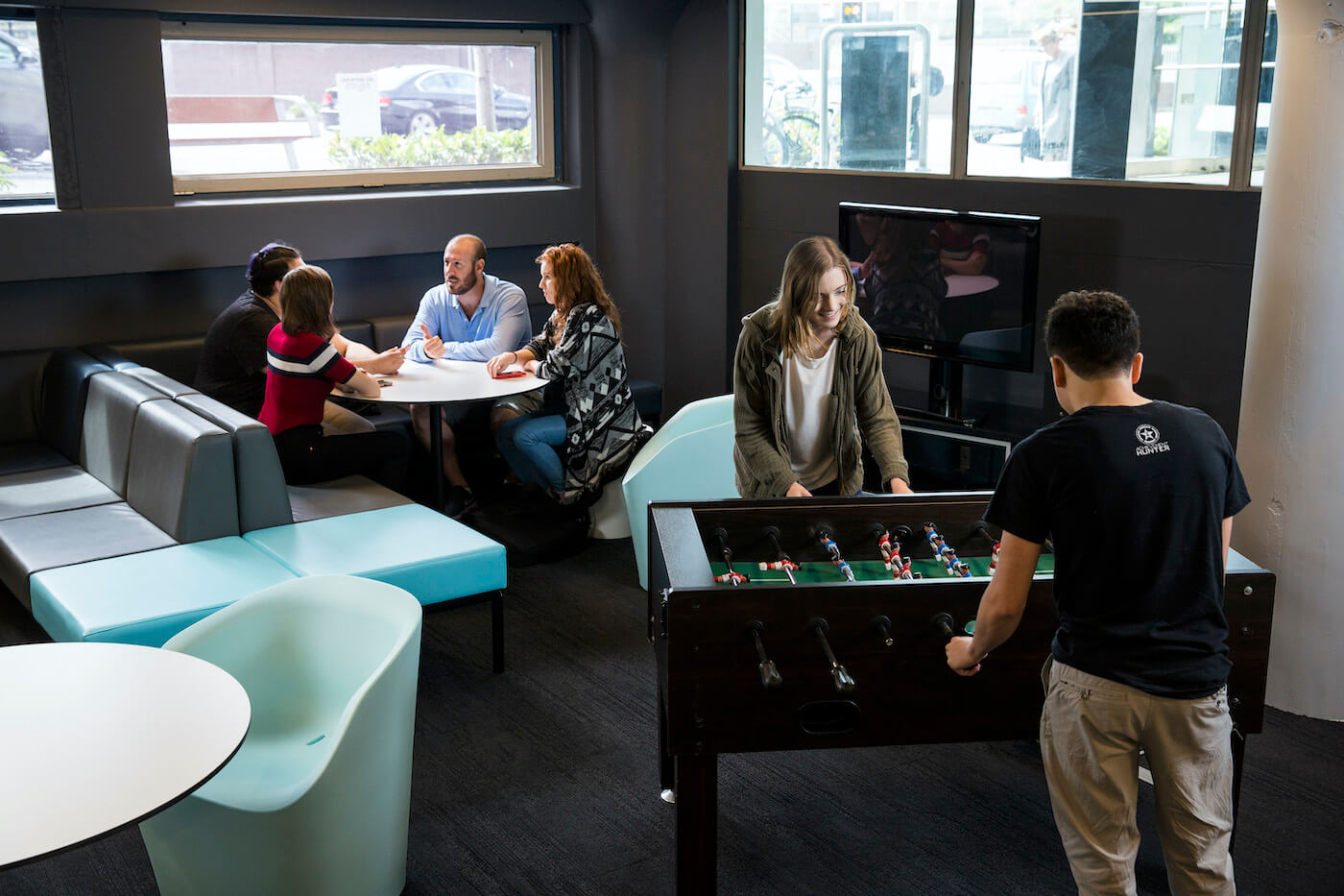 People playing foosball in foreground. Four people sitting at a table behind.