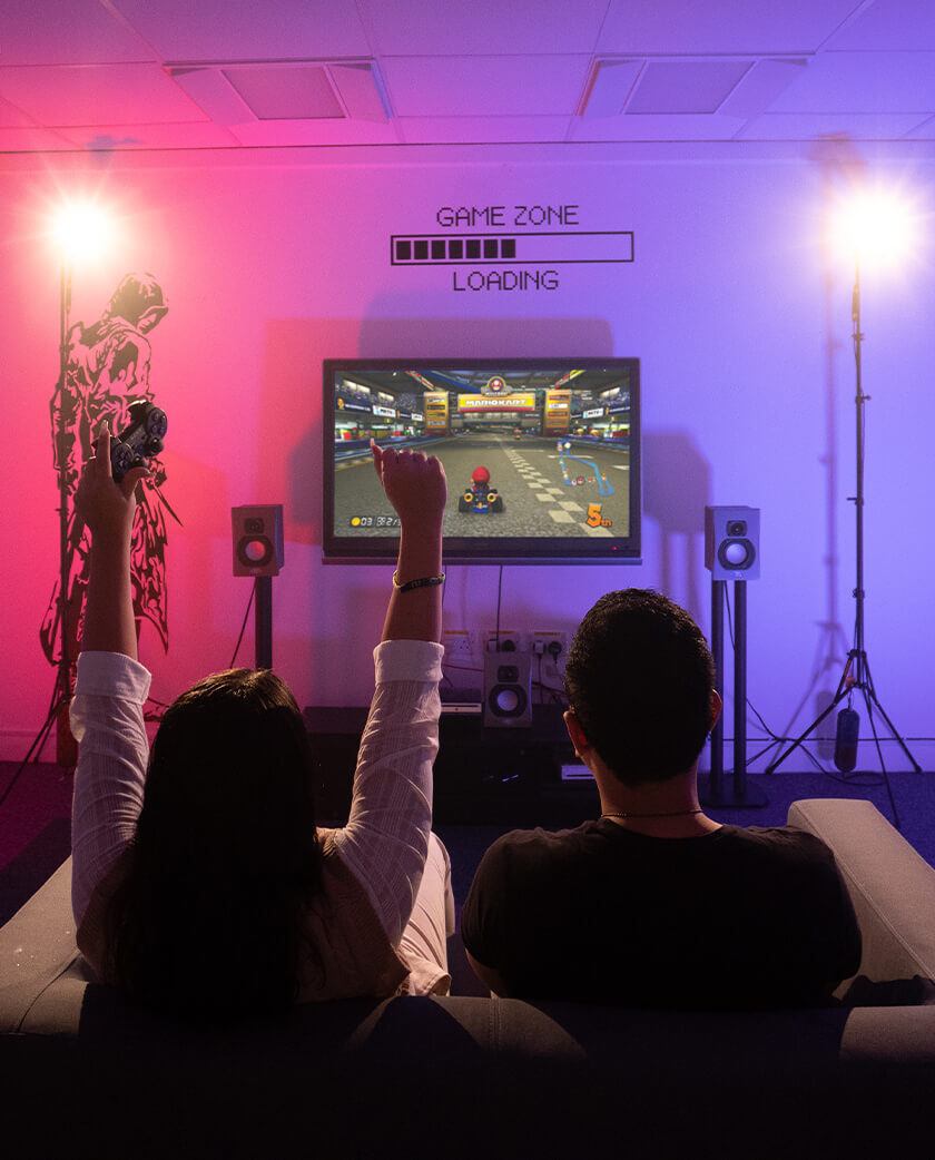 Two students playing video games. Left person has arms up