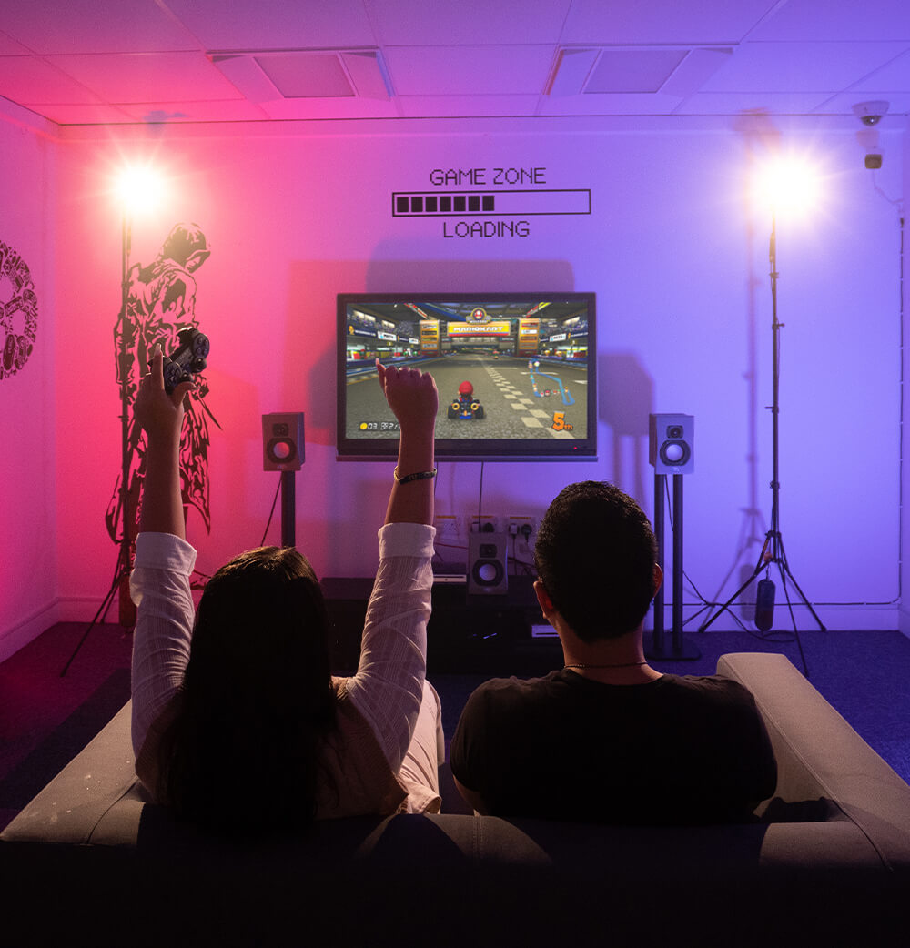 Two students playing video games. Left person has arms up