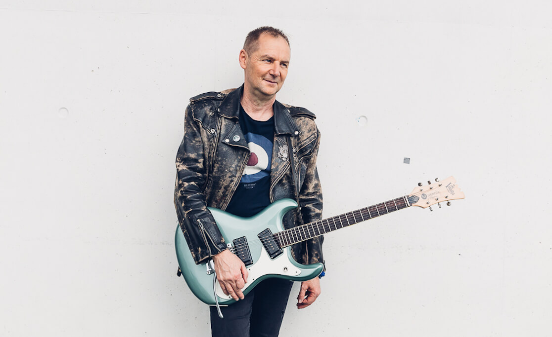 Man wearing leather jacket holding a blue electric guitar