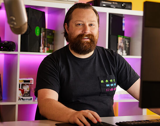 SAE_STAFF_Geoff_Hill Man wearing black tshirt working on computer, looking at camera.