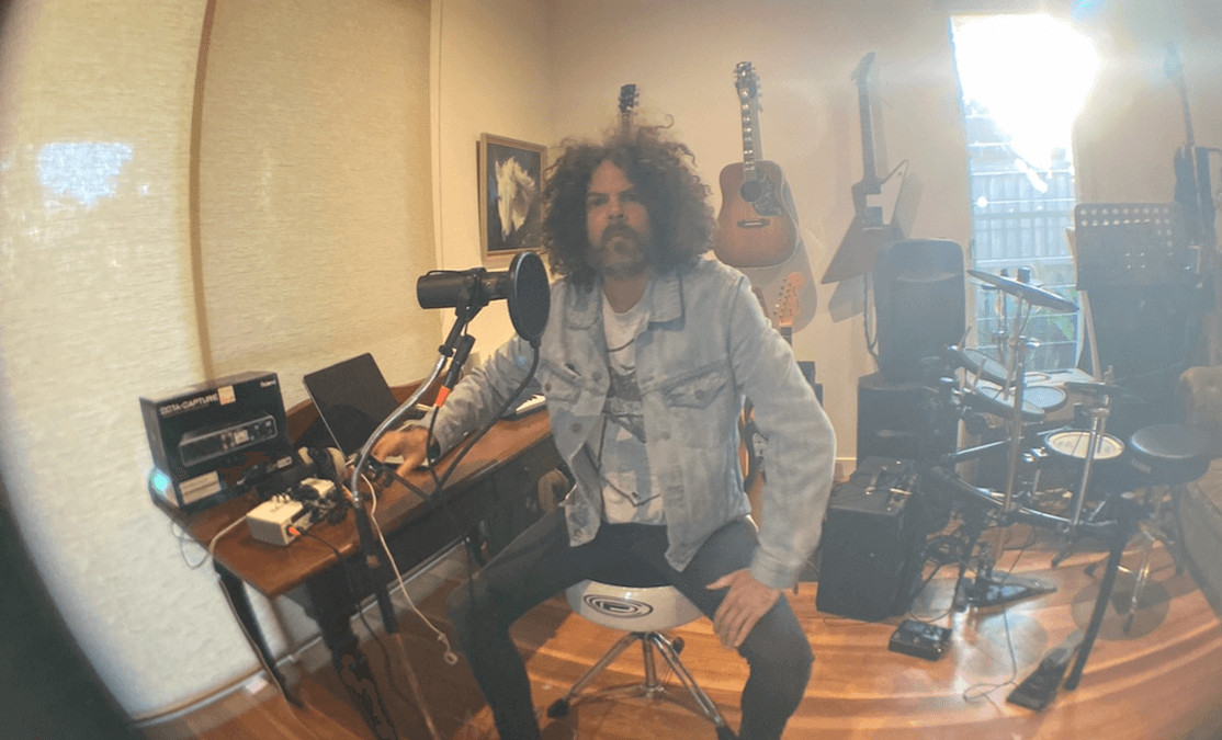 Man with curly hair and beard sitting in a sound studio with instruments. Andrew Stockdale from Wolfmother in recording studio