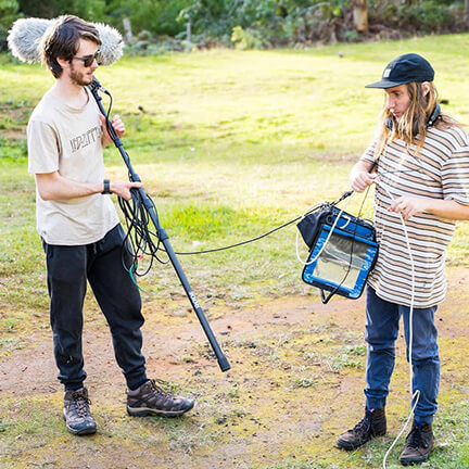 Two students holding sound equipment on set. Around the Sound