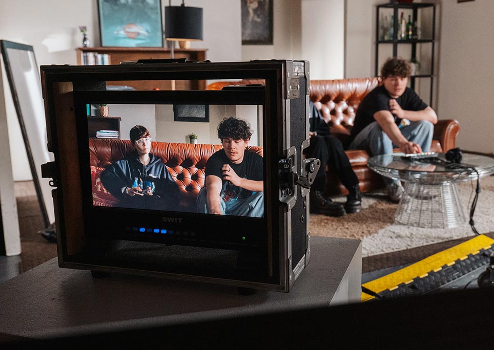 A film camera sitting on a table, with two subjects in the camera frame sitting on a red couch