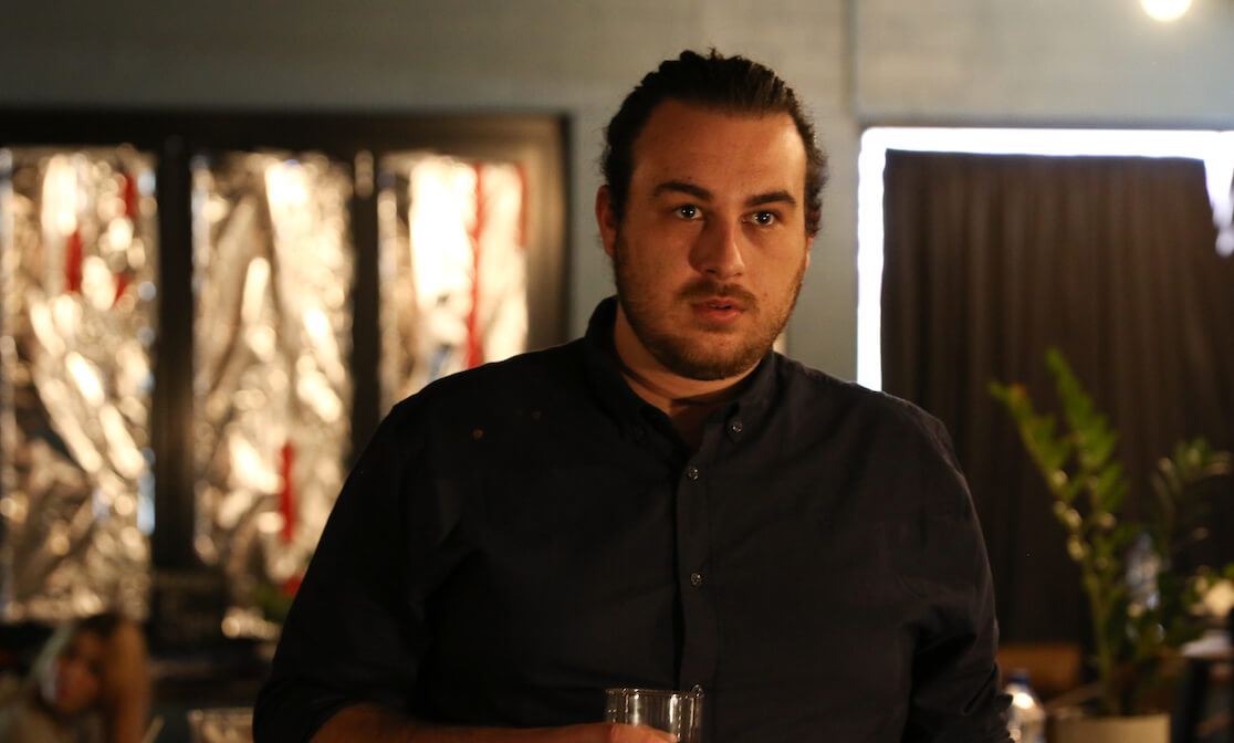 Man with slicked back hair holding a drink. Screenshot from SAE student film Meat.