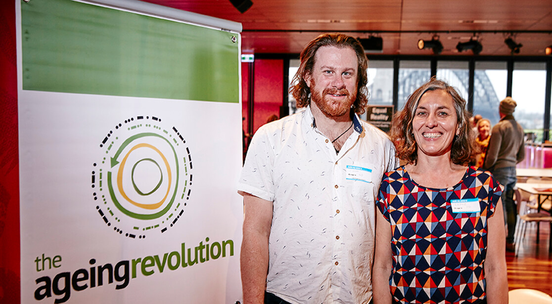 Two people stand in front of a pull up banner that reads "the ageing revolution"