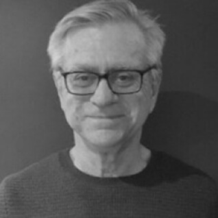A headshot of a man wearing dark rimmed optical glasses and dark crew neck shirt. Dr Richard Vella