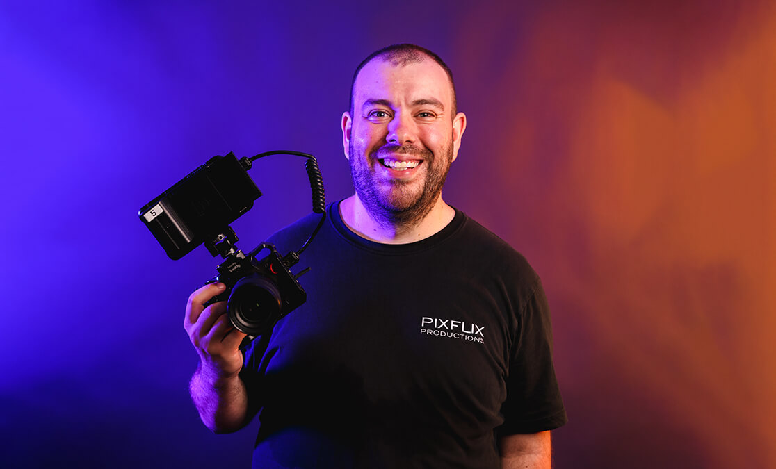 Film graduate Adam Pickstone stands for portrait holding an DLSR with a viewfinder