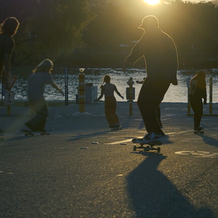 Group of people of skateboards rolling down a hill into the sunset