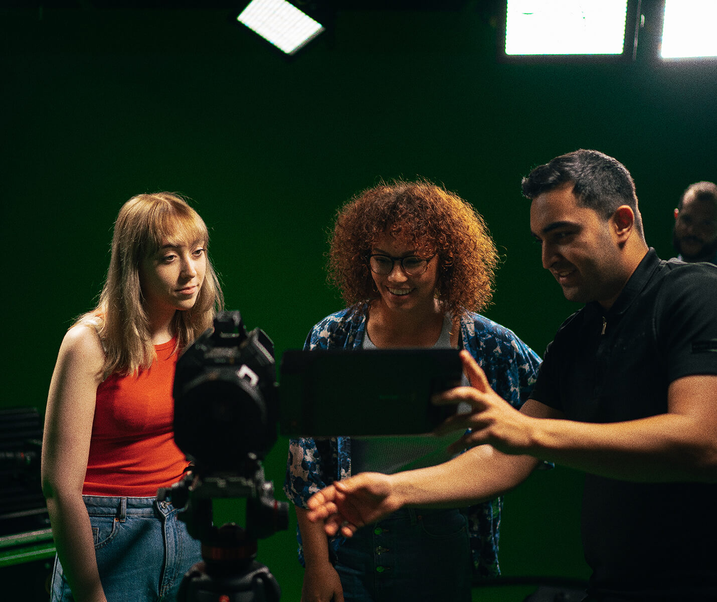 Three students view a camera in a green screen studio