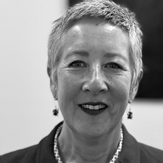 A corporate portrait of dark haired woman wearing a floral shirt. Lucy Schulz