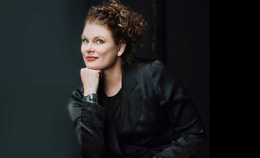 Woman poses to camera, hand under chin.