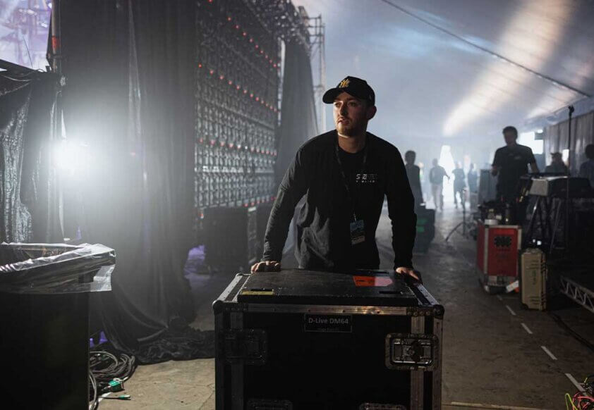 Man pushing audio equipment back of stage at live performance