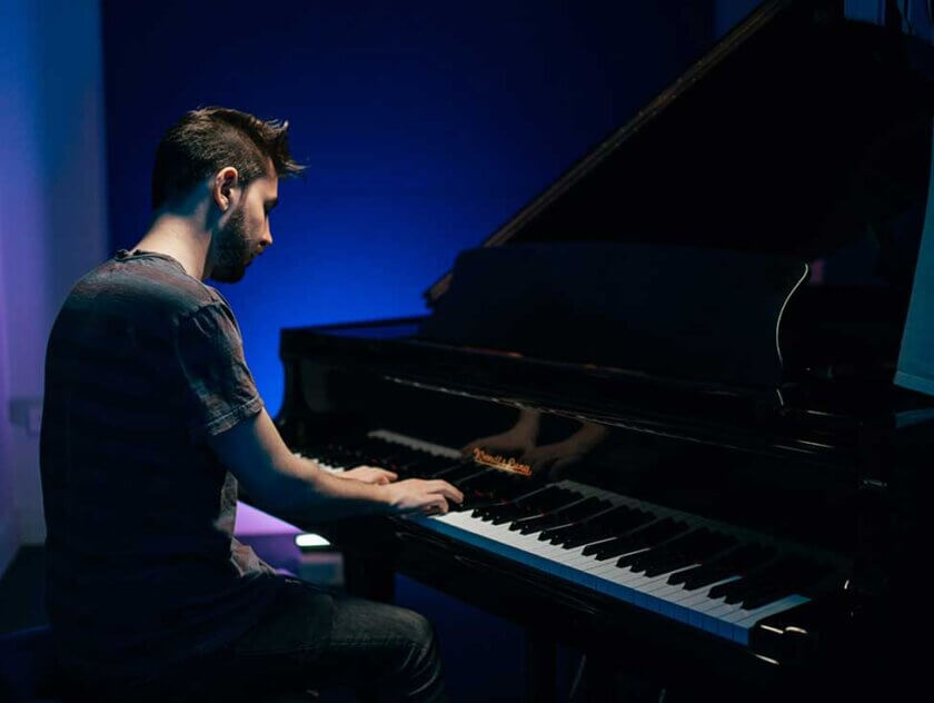 A male music student sits at grand piano in studio
