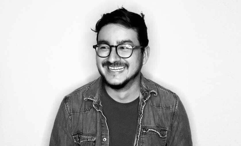 Portrait image of man wearing optical glasses smiling and looking off into the distance. SAE graduate Aldo Arechar