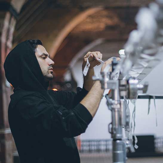 Man wearing a hoodie adjusts the ties of a light screen fixed to a frame on a film set