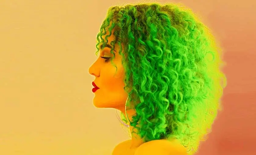 Profile portrait of woman with green curly hair. She wears red lipstick.