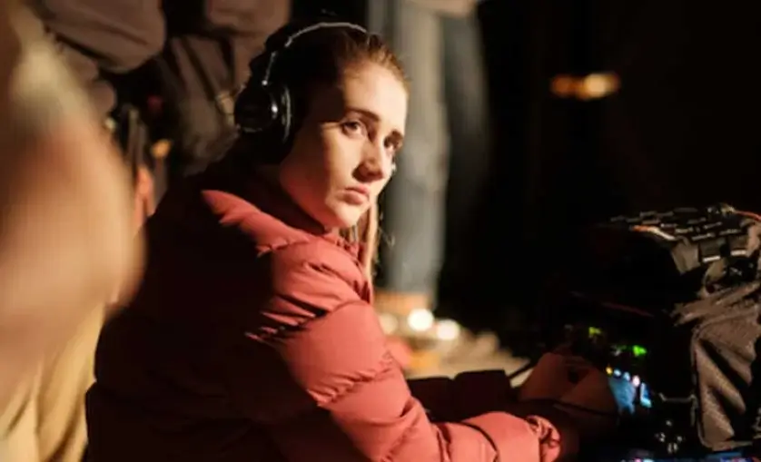 Woman on set with headphones looking over shoulder. Sits in front sound monitor.