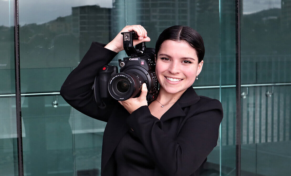 Young woman poses with film camera on her shoulder.