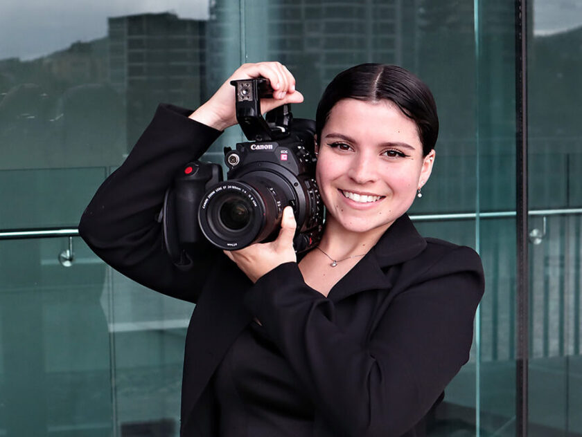Young woman poses with film camera on her shoulder.