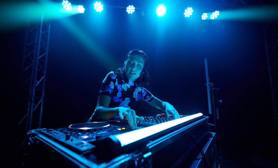 Female DJ mixing music on stage with blue lights shining on her