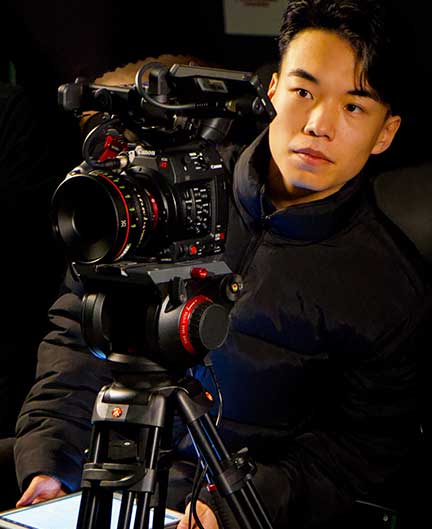 Man stands behind the camera, looking through viewfinder and holding an iPad.