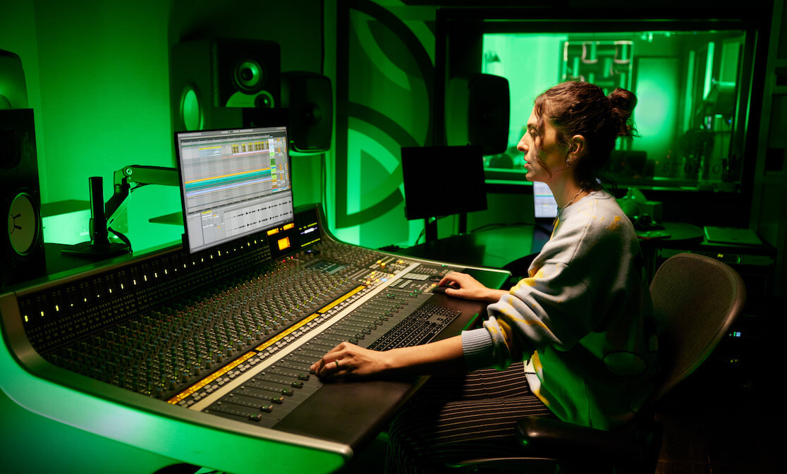 Woman mixing music in a studio with green lighting.