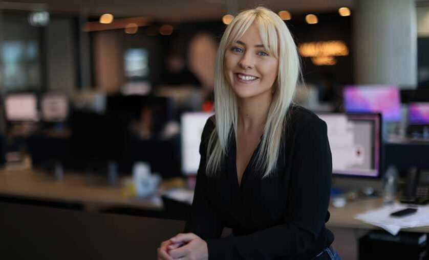 Elly Waite stands at desk and smiles to camera