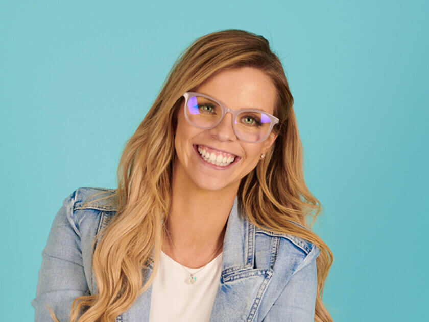 Portrait image of woman in glasses and denim jacket smiling. SAE graduate, Bethany Moran