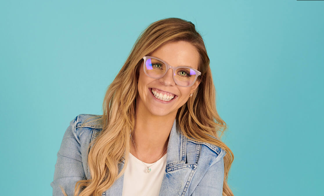 Portrait image of woman in glasses and denim jacket smiling. SAE graduate, Bethany Moran