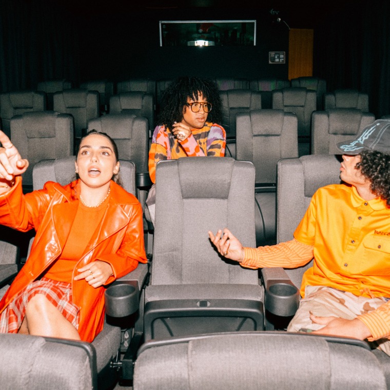 Three students sitting together in a theatre room, with one pointing towards the screen | Film