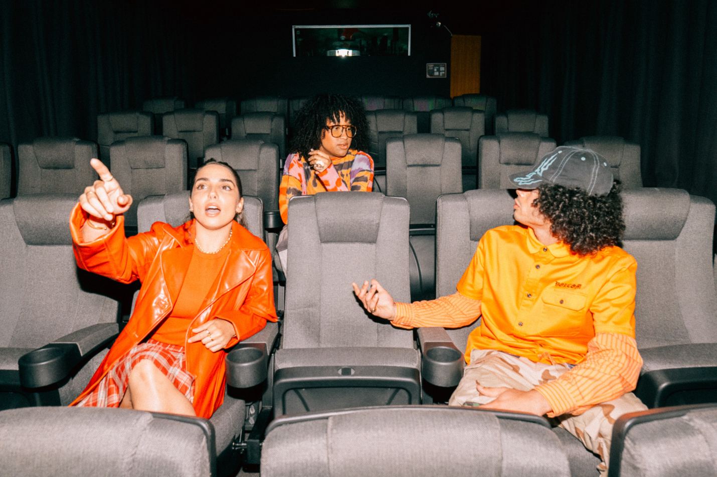 Three students sitting together in a theatre room, with one pointing towards the screen | Film