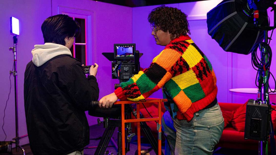 Two students face monitor on camera and on film set.